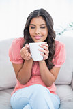 Pleased cute brunette sitting on couch holding mug
