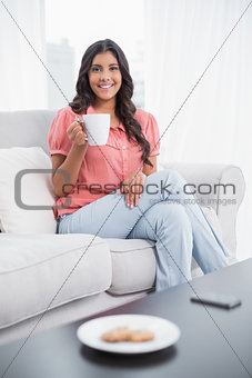 Smiling cute brunette sitting on couch holding mug
