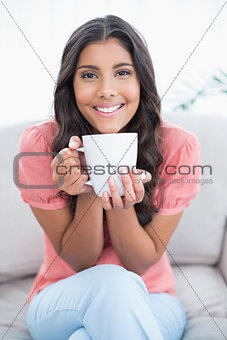 Cheerful cute brunette sitting on couch holding mug