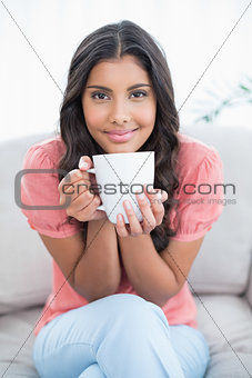 Content cute brunette sitting on couch holding mug