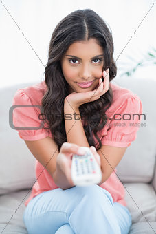 Content cute brunette sitting on couch holding remote