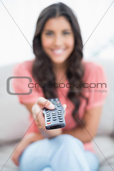 Happy cute brunette sitting on couch holding remote