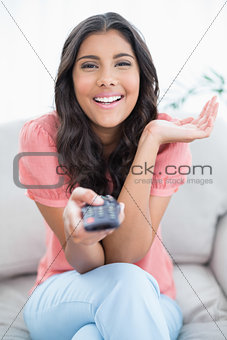 Gleeful cute brunette sitting on couch holding remote