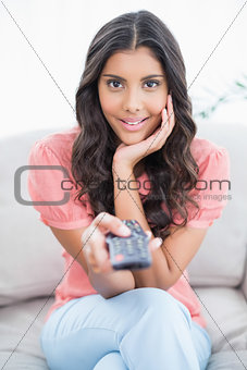 Amazed cute brunette sitting on couch holding remote