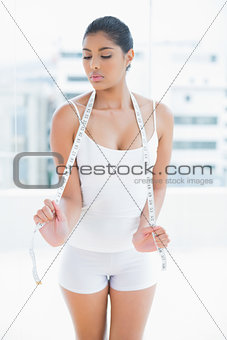 Unsmiling toned brunette holding measuring tape