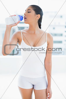 Calm toned brunette drinking from sports bottle