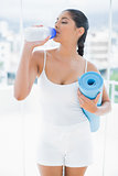 Calm  toned brunette holding sports bottle and exercise mat