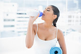 Toned brunette drinking from sports bottle and holding exercise mat