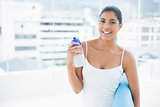 Happy toned brunette holding sports bottle and exercise mat