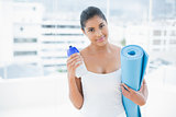 Pleased toned brunette holding sports bottle and exercise mat