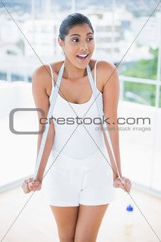 Excited toned brunette holding measuring tape around neck