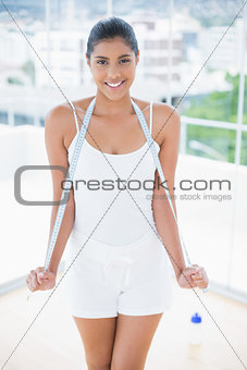 Smiling toned brunette holding measuring tape around neck