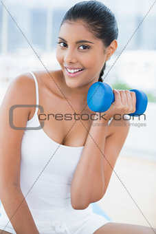 Cheerful toned brunette sitting on floor with dumbbells