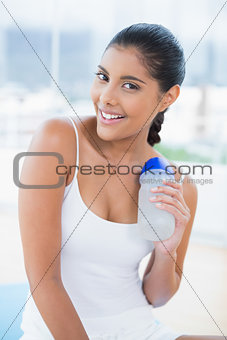 Cheerful toned brunette sitting on floor with sports bottle