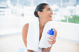 Cheerful toned brunette with towel holding sports bottle