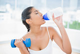 Peaceful toned brunette with dumbbells drinking from sports bottle