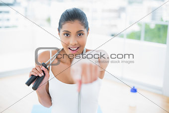Excited toned brunette sitting on floor with skipping rope