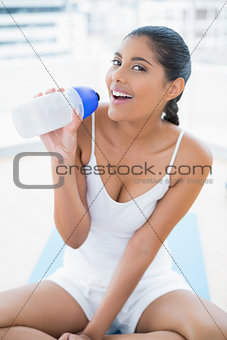 Smiling toned brunette sitting on floor holding sports bottle