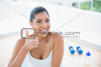 Cheerful toned brunette sitting on floor showing thumb up