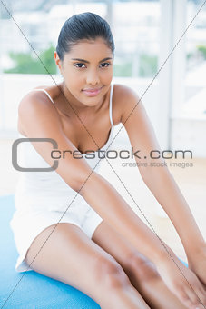 Content toned brunette sitting on floor stretching legs