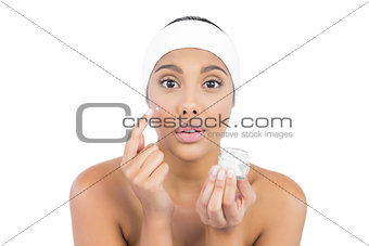 Frowning nude brunette using moisturizer looking at camera