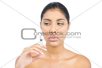 Serious nude brunette holding injection looking at it
