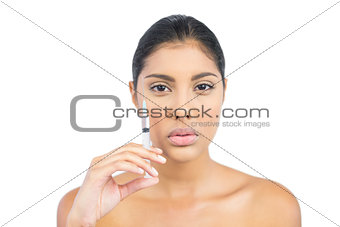 Serious nude brunette holding injection focusing camera