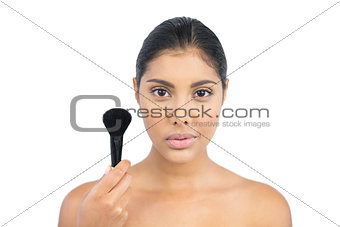 Unsmiling nude brunette holding powder brush