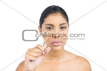 Serious nude brunette holding eyelash curler