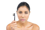 Frowning nude brunette holding eyebrow brush