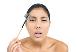 Frowning nude brunette using eyebrow brush