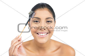 Smiling nude brunette using eyebrow brush
