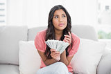 Thoughtful cute brunette sitting on couch holding money