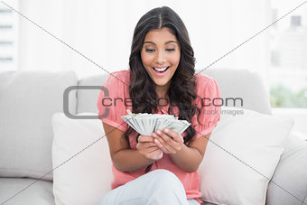 Excited cute brunette sitting on couch holding money