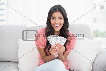 Cheerful cute brunette sitting on couch holding money