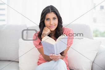 Happy cute brunette sitting on couch reading a book