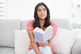 Thoughtful cute brunette sitting on couch reading a book