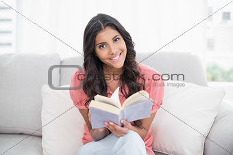 Cheerful cute brunette sitting on couch reading a book