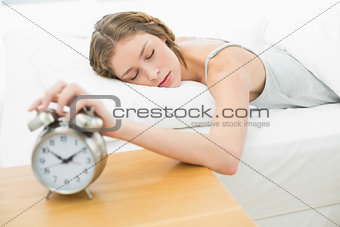 Exhausted young woman turning off the alarm clock
