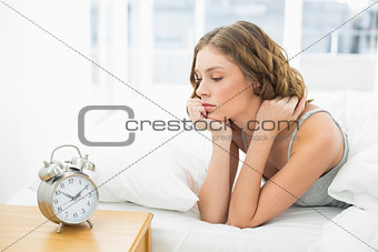 Young woman lying in her bed looking at the alarm clock