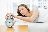 Annoyed beautiful woman turning off the alarm clock while lying in her bed