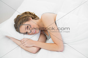 Smiling calm woman lying under the cover on her bed