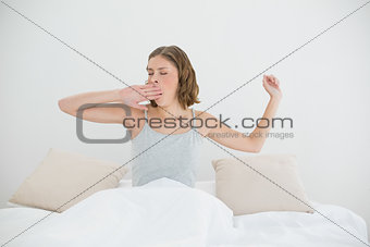 Beautiful woman stretching out and yawning sitting on her bed
