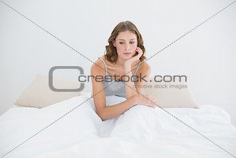 Thoughtful young woman sitting on her bed