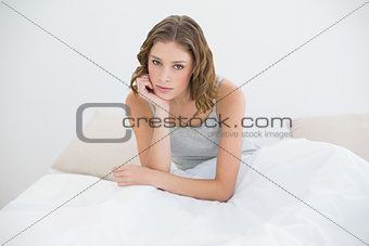 Serious slender woman sitting on her bed under the cover