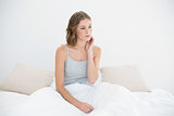 Thoughtful slender woman sitting under the cover on her bed