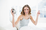 Cheering young woman holding an alarm clock sitting on her bed