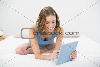Lovely content woman sitting smiling on her bed using her tablet