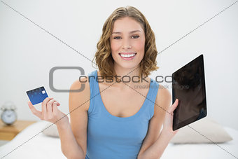Beautiful calm woman showing her tablet and debit card smiling at camera