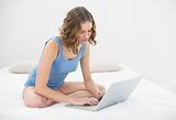 Beautiful serious woman sitting on her bed typing on her notebook